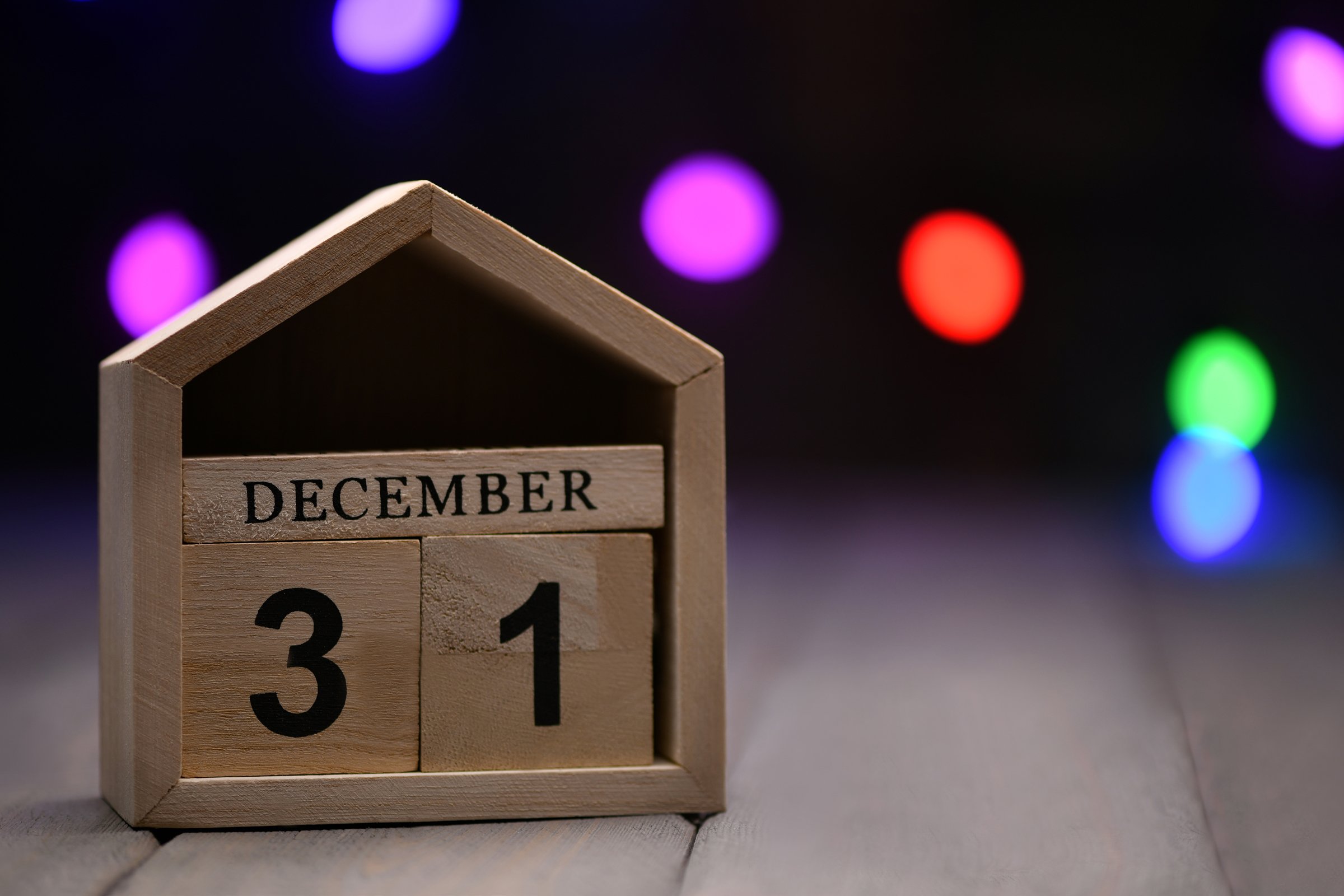 Christmas decorations on a wooden background: wooden cubes with the numbers December 31, and fuzzy multi-colored garland in the background. Selective focus