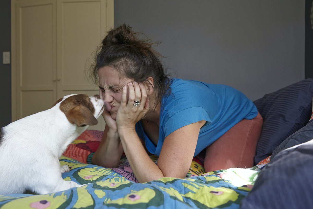 Woman pulling face whilst being licked by dog