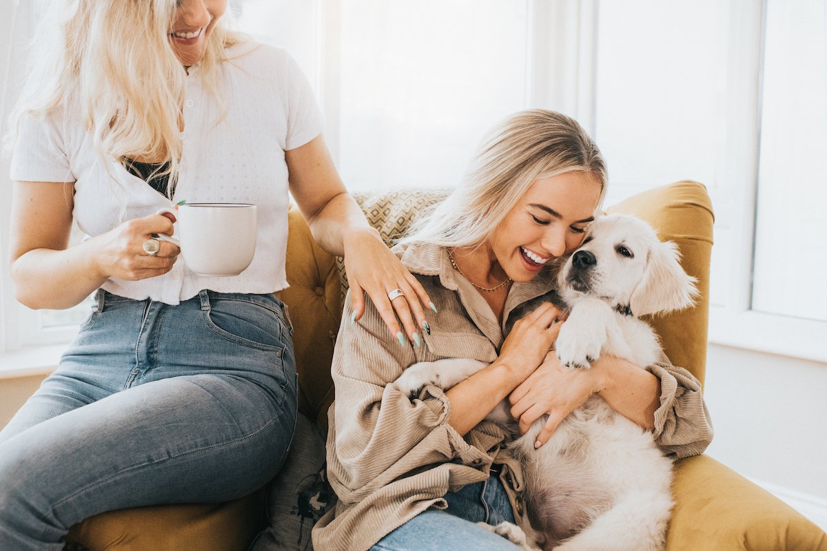 Woman cuddles 12 week old Golden Retriever Puppy while another looks on and smiles