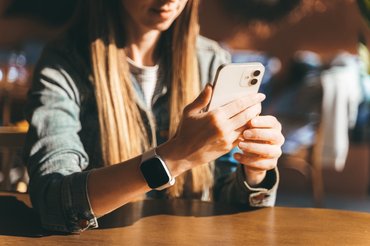 Fiatal nő ül az asztalnál kezében telefonnal