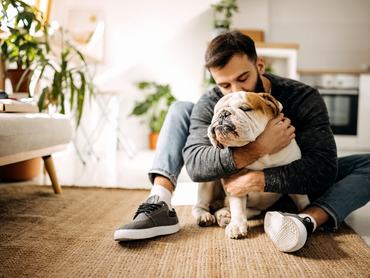 Férfi bulldog kutyát ölel a földön ülve